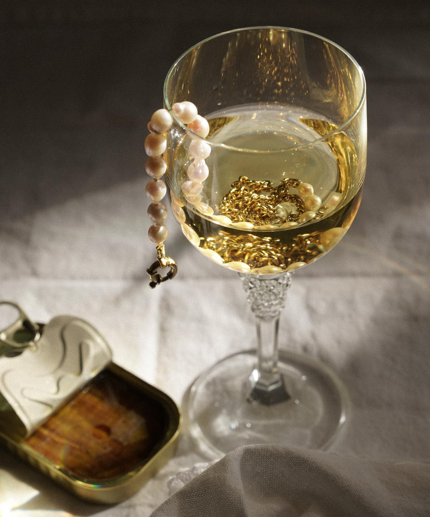 Glas witte wijn met parelketting erin en een blikje ansjovis op tafel